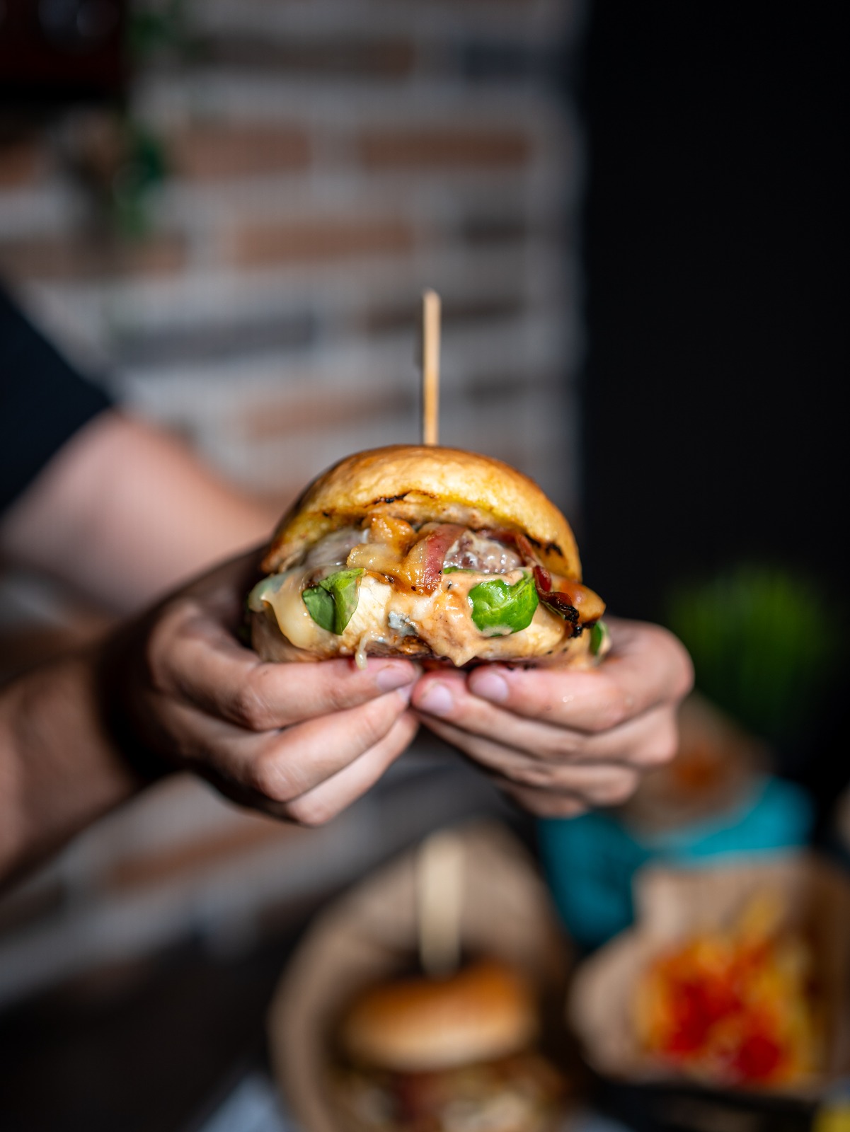 Smash burger s rastopljenim sirom i bambusovim štapićem u ruci gosta